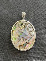 Front view of the oval-shaped sterling silver pendant with large polished abalone shell and decorative leaf accents on the frame.