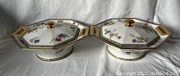 Pair of octagonal covered serving dishes viewed from the front, showing floral design and gold handles.