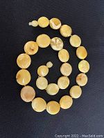 Full view of the coiled necklace showing round, flat egg yolk amber beads in yellow and tan marbled colors on black background.