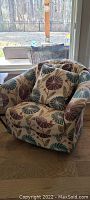 Side view of the rocking swivel accent chair showing the floral patterned fabric upholstery and curved chair shape.