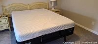Assembled queen size adjustable bed frame with white Sealy mattress and decorative headboard in background