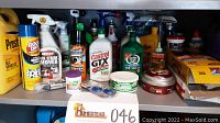 Full view of shelf with collection of automotive fluids, chemicals, and cleaning sprays including antifreeze, oil, and sealant.