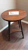 Wooden round side table with turned legs and a paper tag on top showing item number 009.