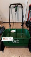 Full view of Scotts Turf Builder Classic Drop Spreader showing green plastic hopper, black wheels, and metal handle with green adjustment knob.