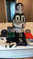 Full lot view showing Seahawks inflatable punching bag, Mariners bobbleheads, various shirts, hoodies, cap, pet dish, and tote bag