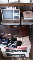 Unboxed TRS-80 Model III on shelf with boxed unit beneath and manuals in front