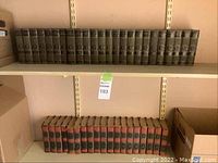 Two shelf levels showing two collections of hardcover books. Upper shelf has 19 volumes with green covers and gold decorations by Charles Dickens (1930). Lower shelf has 26 volumes with green covers and gold embossing by Mark Twain (1917).