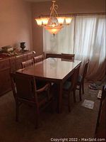 Full view of vintage solid wood dining table with 6 matching chairs in room setting under chandelier, with glass top on the table.