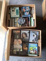 Two boxes filled with assorted DVDs and Blu Rays. Visible titles include Shrek, March of the Penguins, Premonition, Vacancy, Miss Potter, and The Love Song of Bobby Long.