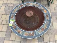 Top view of the fire pit showing the decorative tile border and mesh cover on top.