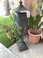 Front and side view of the iron mailbox showing the relief sculptures, pedestal, and finial top.