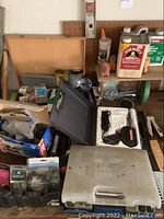 Photo showing assorted tools and furniture finishing chemicals including bottles of Formby's furniture refinisher and wood glue, a white plastic case with a soldering iron, and other tools and supplies on a workbench.