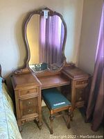 Front view of vintage solid wood vanity with large decorative mirror and matching bench beneath it.