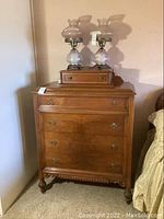 Photo showing solid wood vintage dresser with four drawers and caster wheels, small drawer box, and two glass oil lamps on top