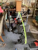Weight bench with disc weights, power resistance stack, and yoga mat secured with a green strap; located in a garage setting.