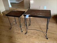Two wooden and metal nesting tables on wooden floor, showing top surfaces and metal legs with curved designs.