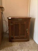 Front angle view of wooden side table cabinet against wall near a desk.