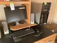 Wide view of the Dell XPS desktop tower, 18 inch Dell monitor on a wooden desk, grey/silver speakers on each side of the monitor, Dell keyboard and mouse on black desk mat.