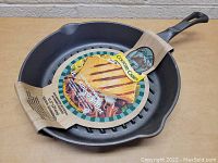 Image showing the 11.5 inch Country Cabin cast iron skillet pan from a top front angle with packaging intact, placed on a wooden surface.