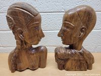 Front profile view of two vintage carved wood busts highlighting facial features and hairstyles.