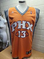 Front view of Adidas Phoenix Suns basketball jersey with embroidered PHX and number 13 on display, showing orange color and gray side panels