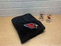 Folded black Cardinals blanket with embroidered logo and two vintage Cardinals collector glasses.