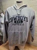 Front view of gray Dallas Cowboys hooded sweater with embroidered text "PROPERTY OF COWBOYS XXL FOOTBALL" and front kangaroo pocket