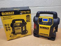 DeWalt jump starter unit with original box, side view showing handle and body with box on left.