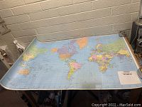 Map spread flat on a table showing world continents and countries with visible laminated surface and size around 32x50 inches.