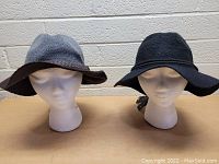 Two women's floppy hats displayed on white mannequin heads. One gray with brown brim, one black with black band.