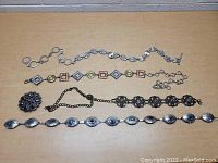 Overview of five women’s decorative belts arranged flat on a tabletop showing various metal link and chain designs plus ornate buckle.