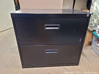 Front view of the black metal lateral file cabinet showing two drawers with recessed handles and lock on top drawer.