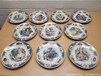 Overview photo showing all 10 porcelain collector plates arranged on table. Each plate has detailed colorful fairytale scene with blue and gold wide border and gold trim.