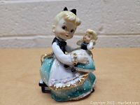 Front angled view of vintage Lefton figurine showing the girl holding the doll, highlighting the detailed facial features and gold accents on the dress.