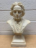 Front view of the Ludwig Von Beethoven bust sculpture on a pedestal base against a white brick background