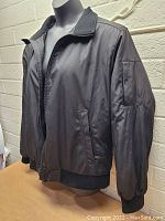 Black insulated Calvin Klein women's jacket displayed on mannequin, showing front and side zippered pockets, ribbed cuffs, and collar.
