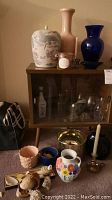 Photo of Mid Century cabinet with sliding glass doors and assorted vases and decorative items including shells, brass bucket and candle holder.
