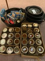 Full view of lot including packed glass jars in two boxes, black canning pot, roasting pots with lids, and boxes of new lids.