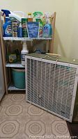 Cleaning products and box fan displayed with wooden shelf unit
