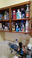 Open cabinet shelves showing multiple cleaning products including sprays and liquid bottles with various brands including Lysol, Vim, and others.