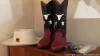 Photo shows ladies cowboy boots in red and black leather with white star and bull head details, white straw hat with Canada pin, and bolero ties in a clear plastic bag.