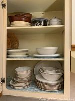 View of cupboard with Meakin oven-to-tableware dishes stacked, wooden bowls on top shelf, dog dish, and covered casserole.
