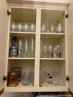 Full cupboard with multiple shelves of assorted glassware including stemware, whiskey glasses, and beer steins.