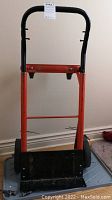 Front view of the orange metal frame hand truck with black handle and boot tray.