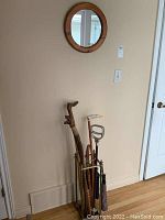 Overall view of walking sticks, umbrellas, standing seat, and holder placed against the wall under the round mirror