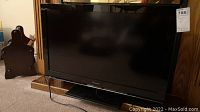 Full frontal view of Panasonic 32-inch flat-screen TV on a carpeted floor with visible electrical cord and nearby wooden furniture.