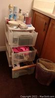 Photo of sole white plastic storage drawer unit with contents visible in drawers and top surface including aerosol sprays, soaps, mugs.