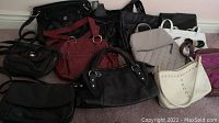 Lot of 12 assorted leather and leather-like purses of various colors, styles and sizes grouped together on the floor.