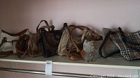 Side view of nine assorted purses on a shelf showing various sizes, colors, and materials