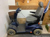 Side view of navy blue four-wheel scooter showing foot platform, wicker basket, and padded seat